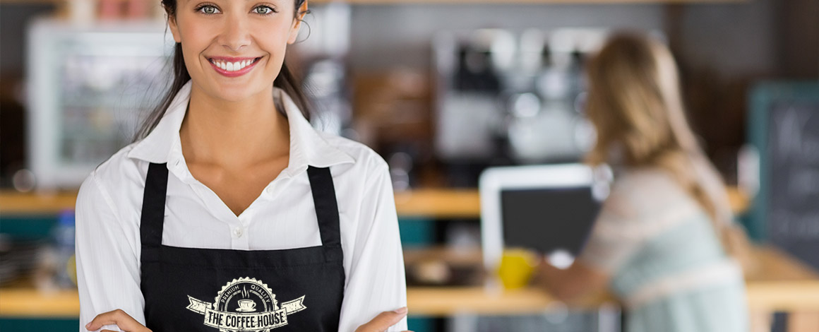vrolijke dame met bedrukte schort staat in haar horeca zaak
