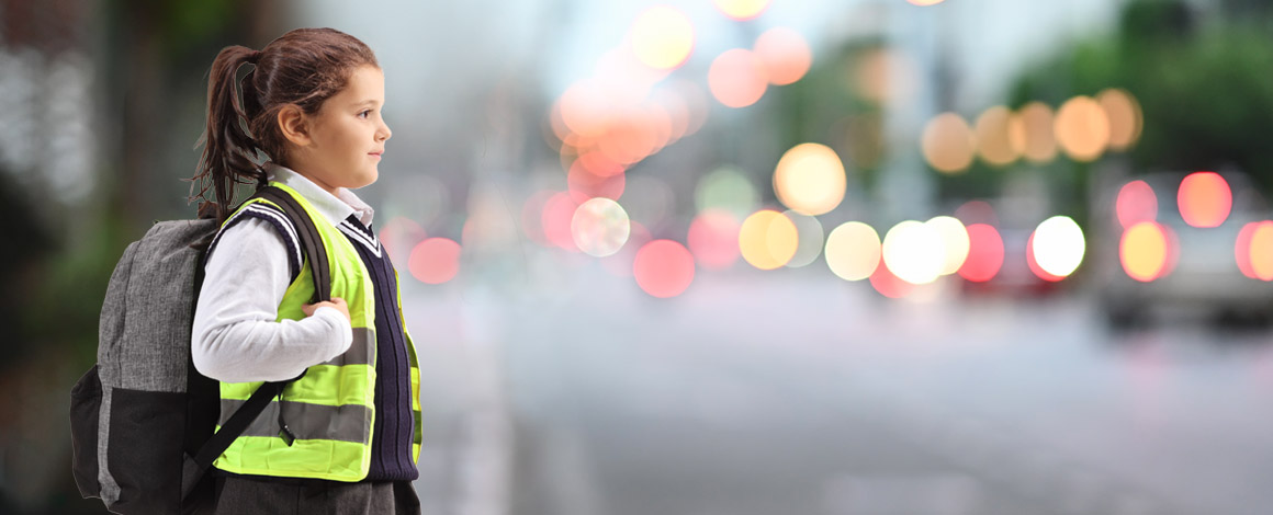meisje wandelt in fluohesje en met boekentas op de rug over een drukke straat