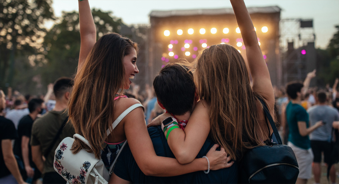 3 jongeren zijn op een festival naar het podium aan het kijken terwijl de avond valt
